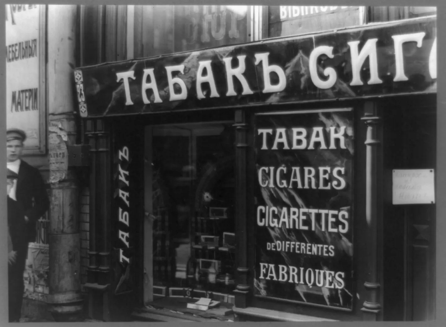 Damaged glass is visible in a tobacco shopfront bearing Cyrillic and French signs.