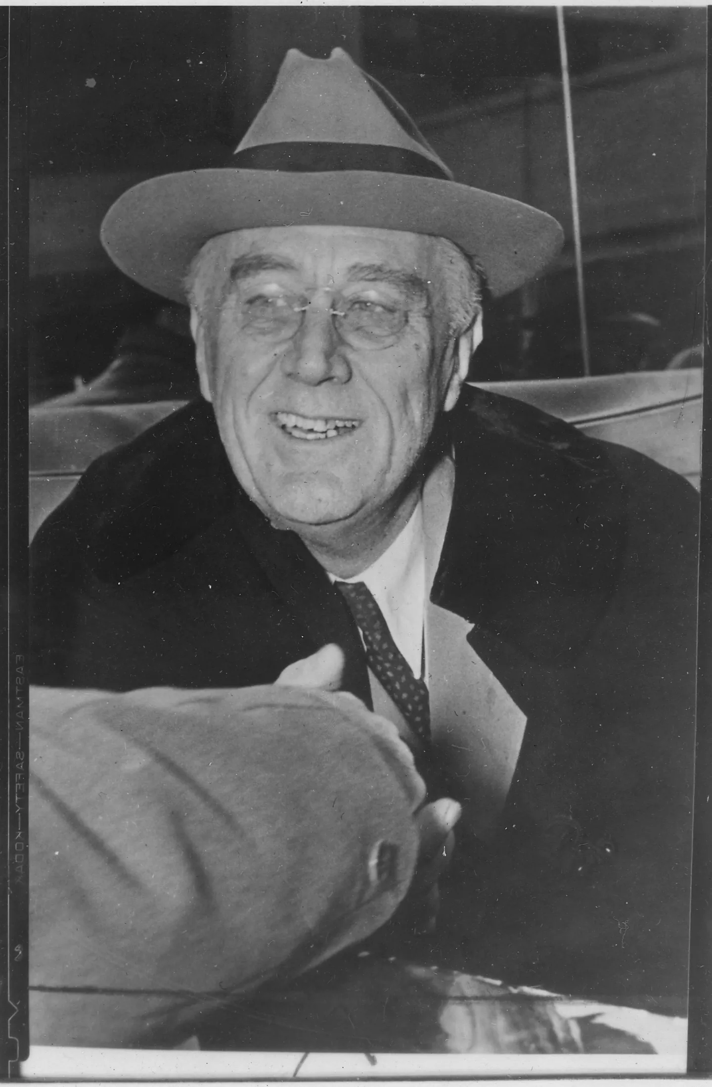 Roosevelt smiles while wearing a broad-brimmed hat and overcoat.