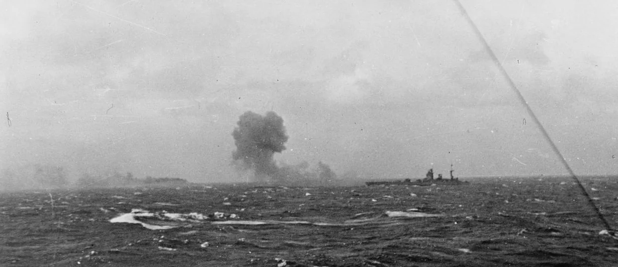 Distant silhouette of HMS Rodney at right during the final battle, with a large smoke cloud over Bismarck farther left across rough water.