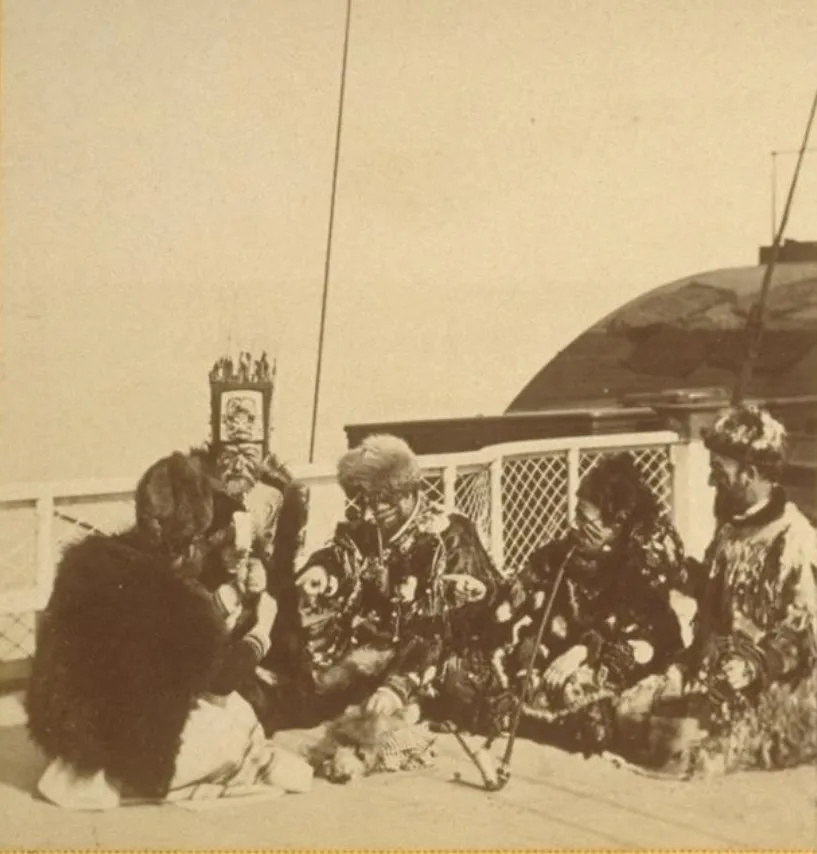 A group of Indigenous people seated together at Sitka, wearing distinctive robes and headgear.