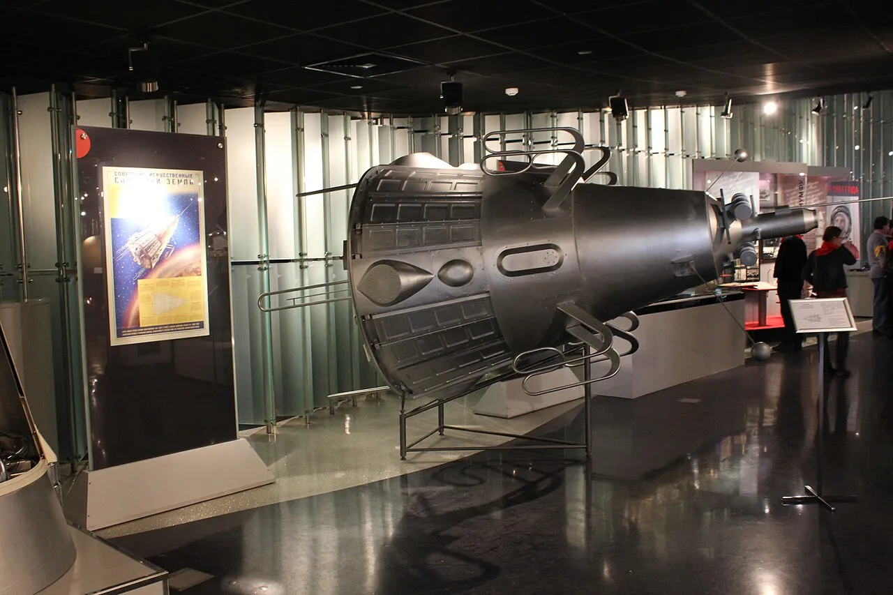 A large Sputnik 2 model displayed horizontally beside museum panels and visitors.