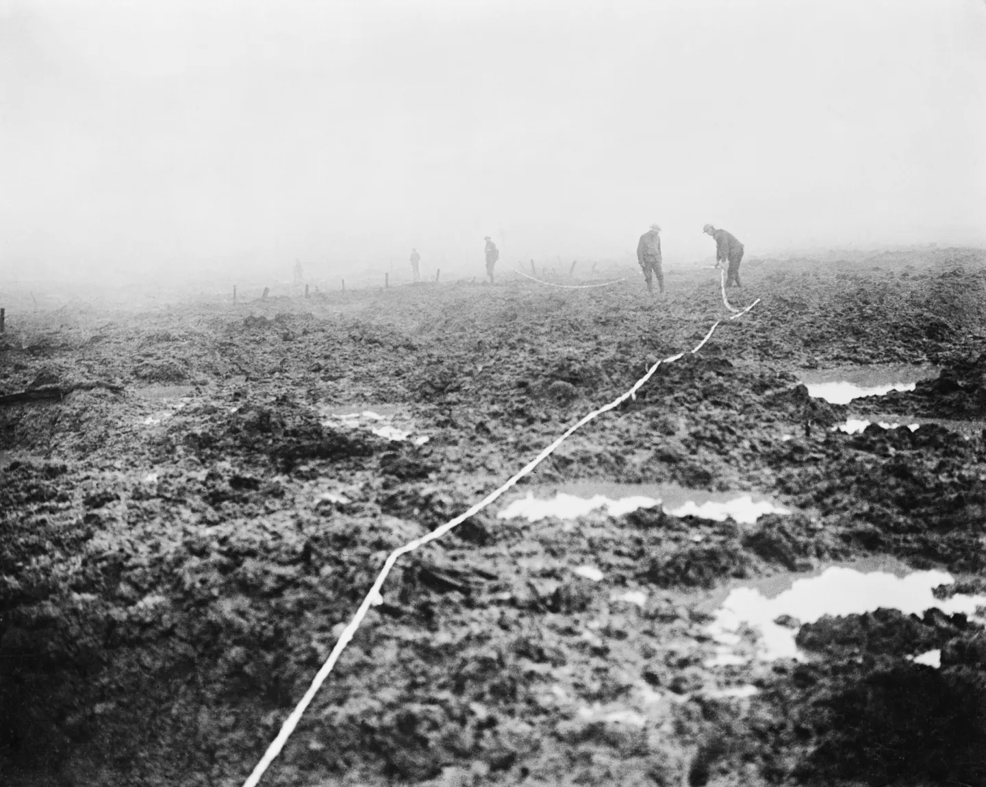 Canadian pioneers laying a narrow strip of tape across muddy ground.