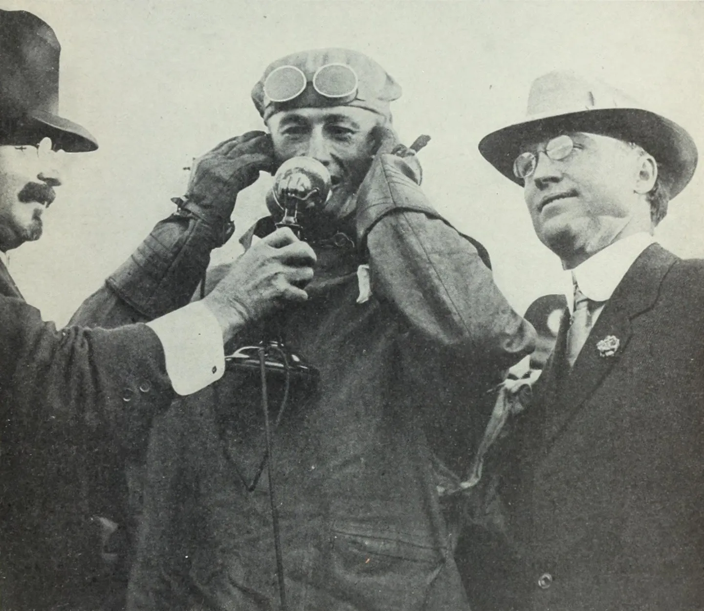 Rodgers drinking from a bottle while men stand beside him.
