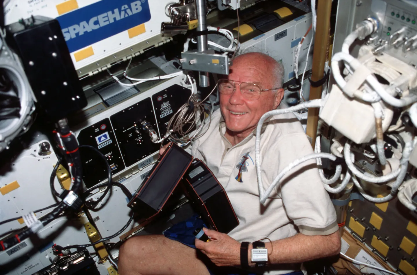 John Glenn moves experiment cartridges in the Spacehab laboratory.