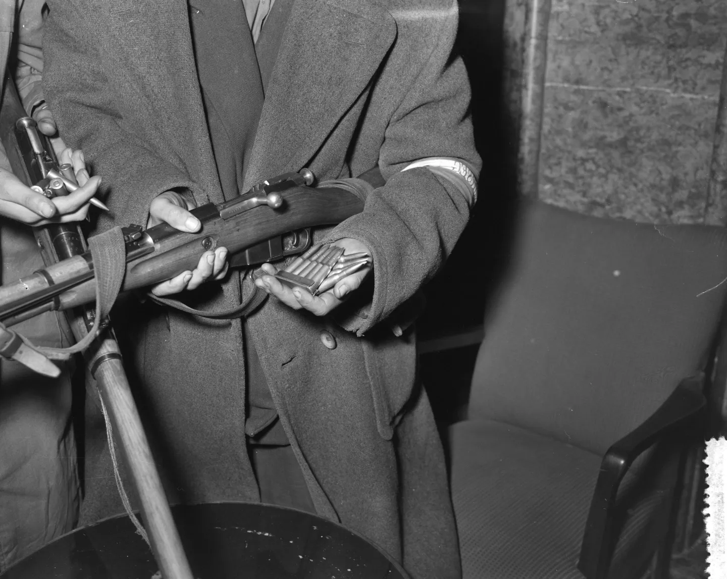 A man holds loose rifle cartridges beside a bolt-action rifle.