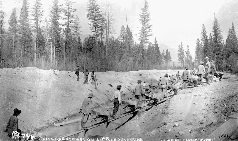 Chinese railway workers stand and work along an excavated roadbed amid trees.