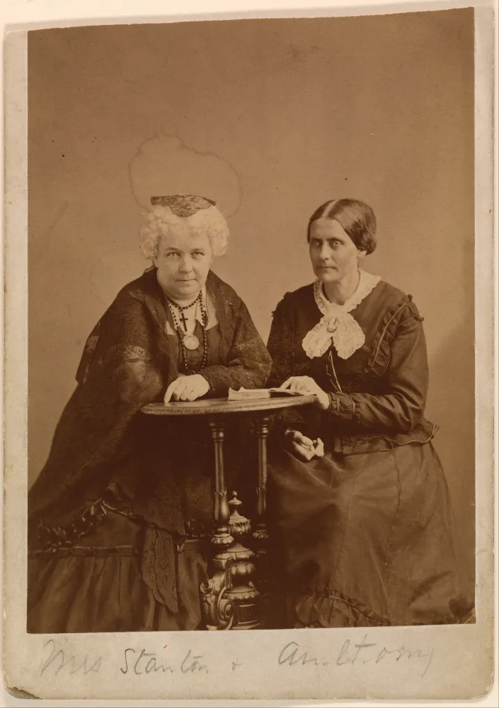 Elizabeth Cady Stanton and Susan B. Anthony seated together beside a table.
