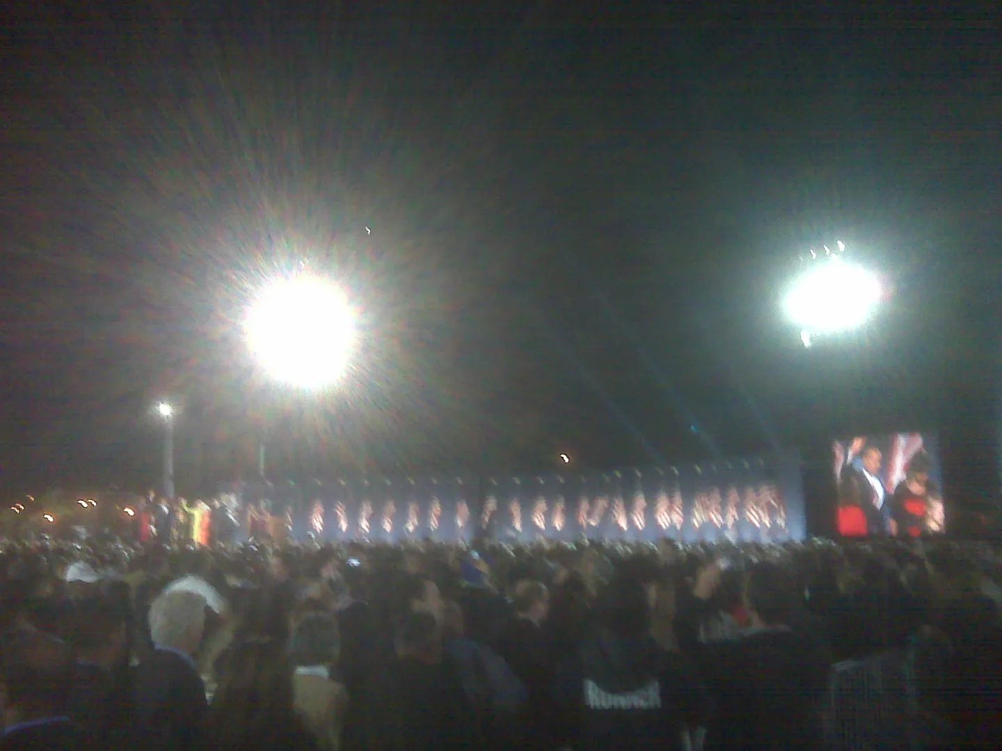 The Obama family appearing on a distant screen beside the illuminated Grant Park stage.