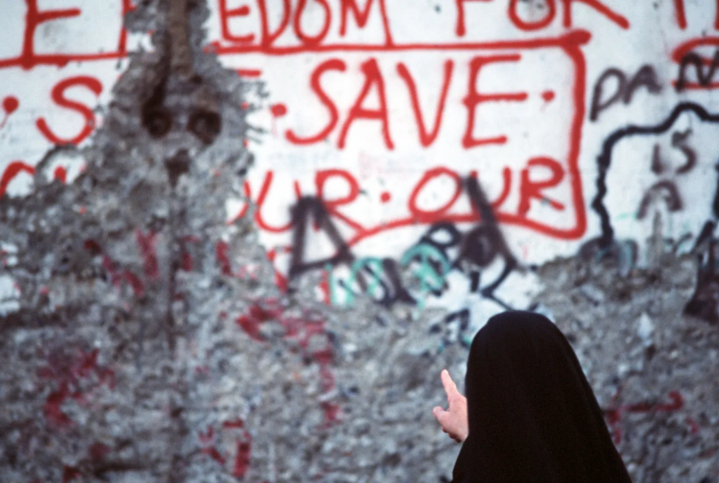 A nun standing beside and studying graffiti on a surviving section of the Berlin Wall.