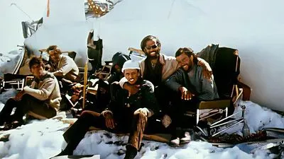 Survivors sitting in snow beside the torn fuselage and exposed seat frames of Flight 571 in the Andes.