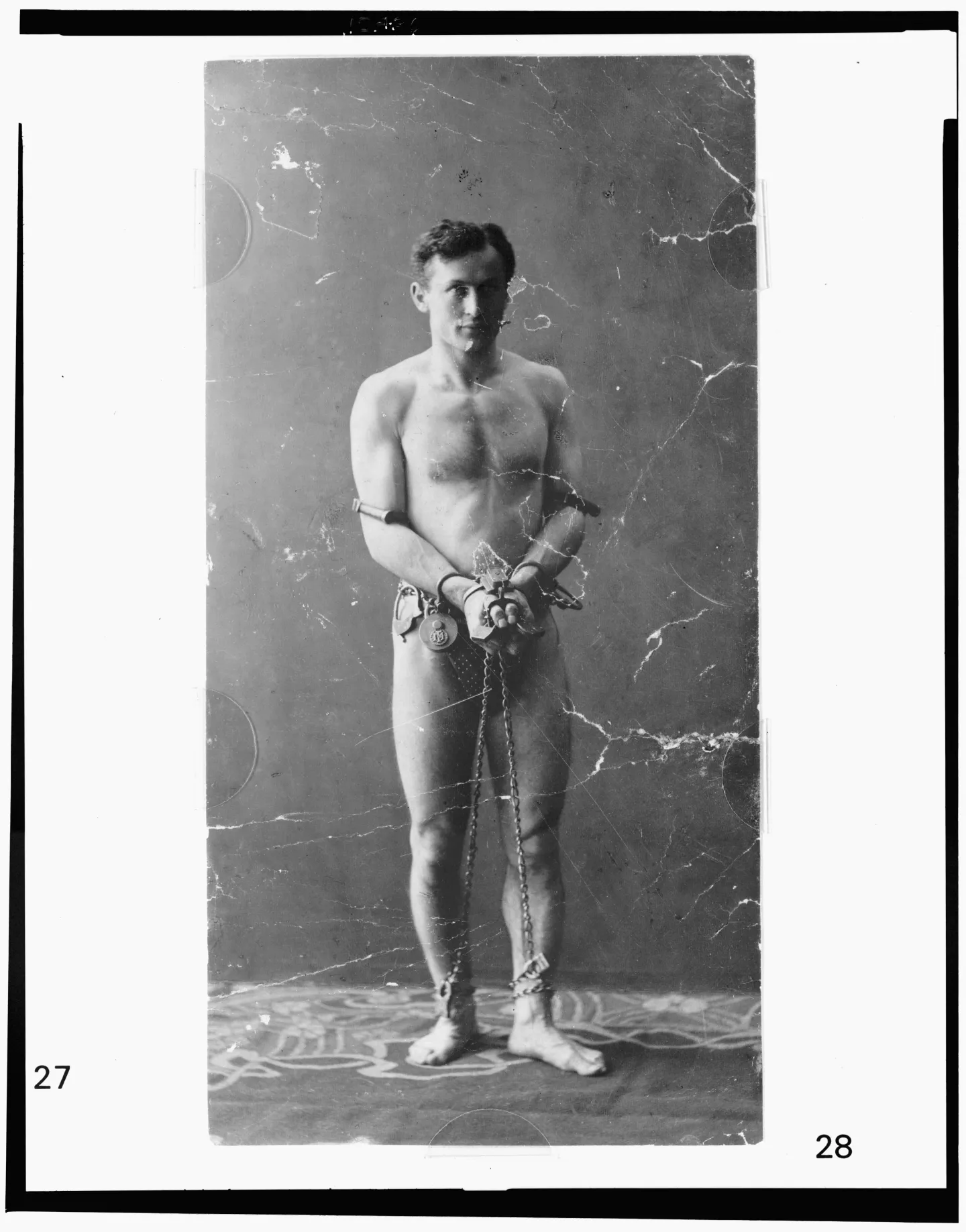 Houdini stands facing the camera with chains around his body.