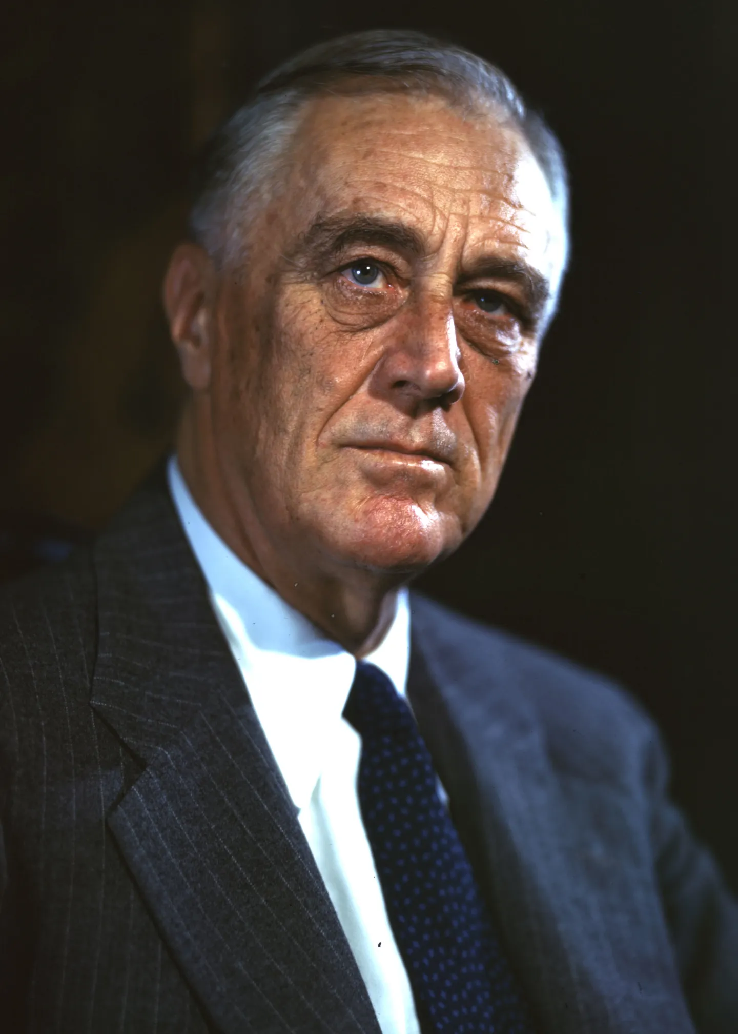 Color portrait of Roosevelt wearing a dark jacket and tie against a dark background.