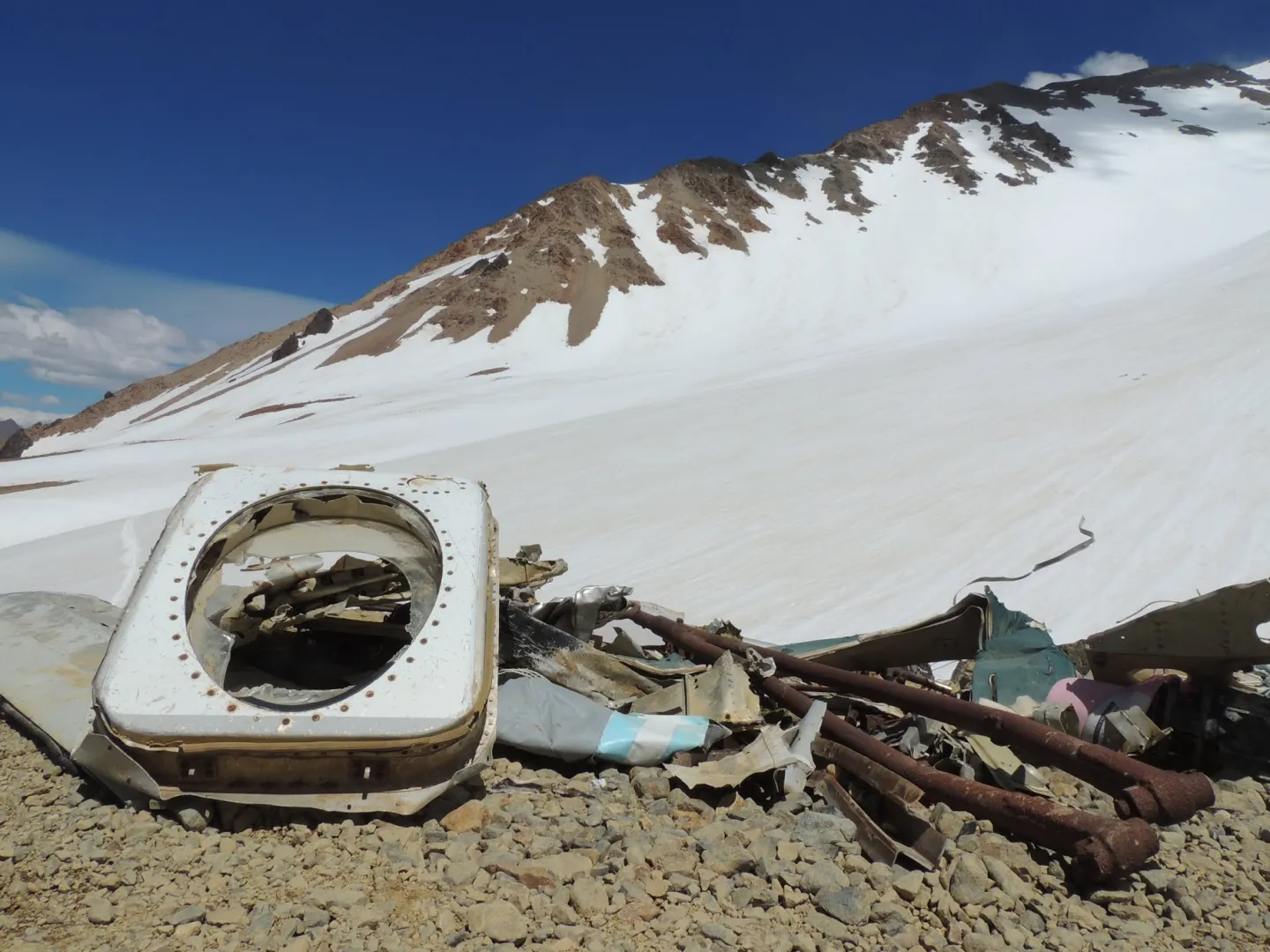 A rounded aircraft window frame and twisted fragments of Flight 571 lying below a snow-covered Andean slope.