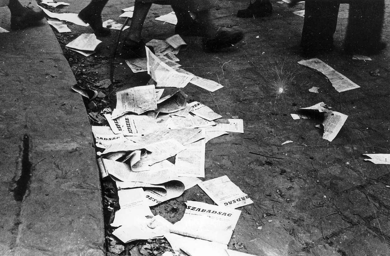 Torn copies of the November 13, 1956 issue of Népszabadság scattered beside a curb.