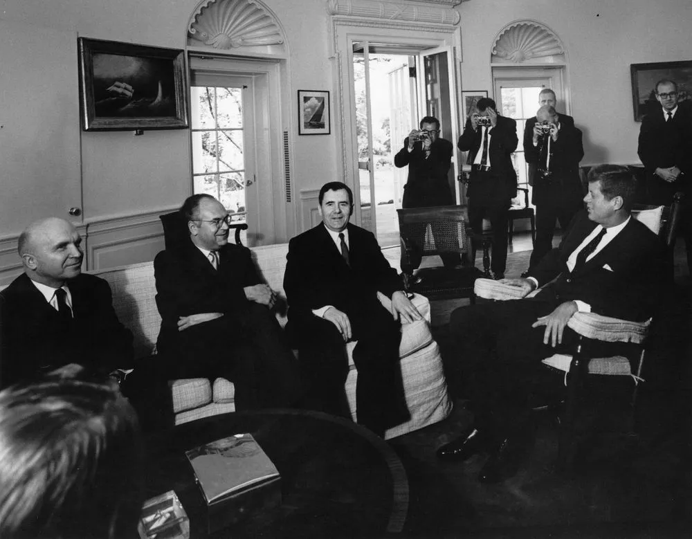 President Kennedy seated opposite Soviet Foreign Minister Andrei Gromyko and other Soviet officials, with press photographers behind them in the Oval Office.