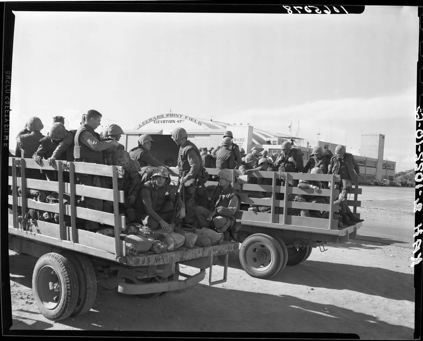 U.S. Marines with helmets and packs sitting on open trailers in front of the Leeward Point Field hangar at Guantánamo Bay.