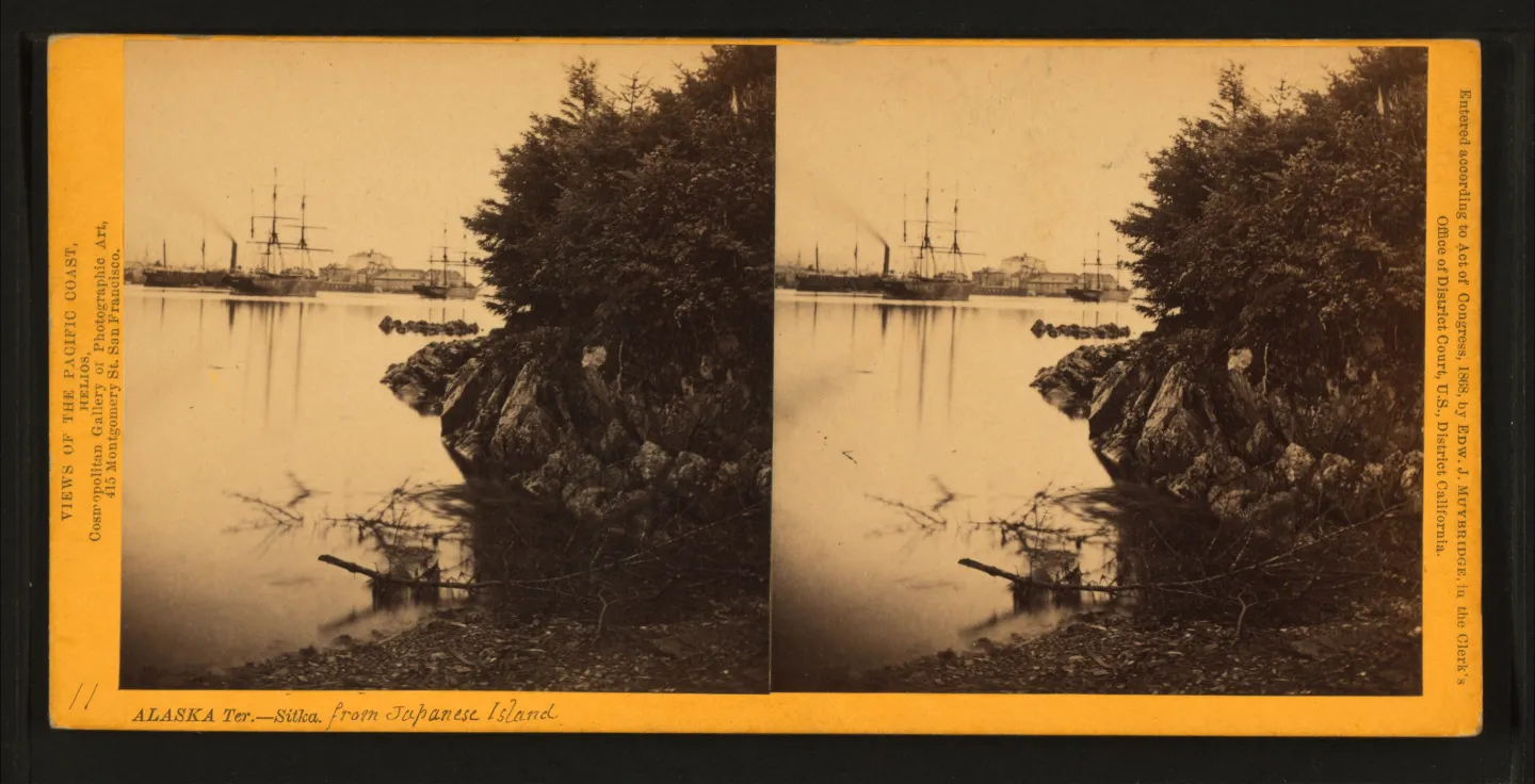A yellow-mounted stereoscopic card with two views across Sitka’s harbor from Japanese Island.