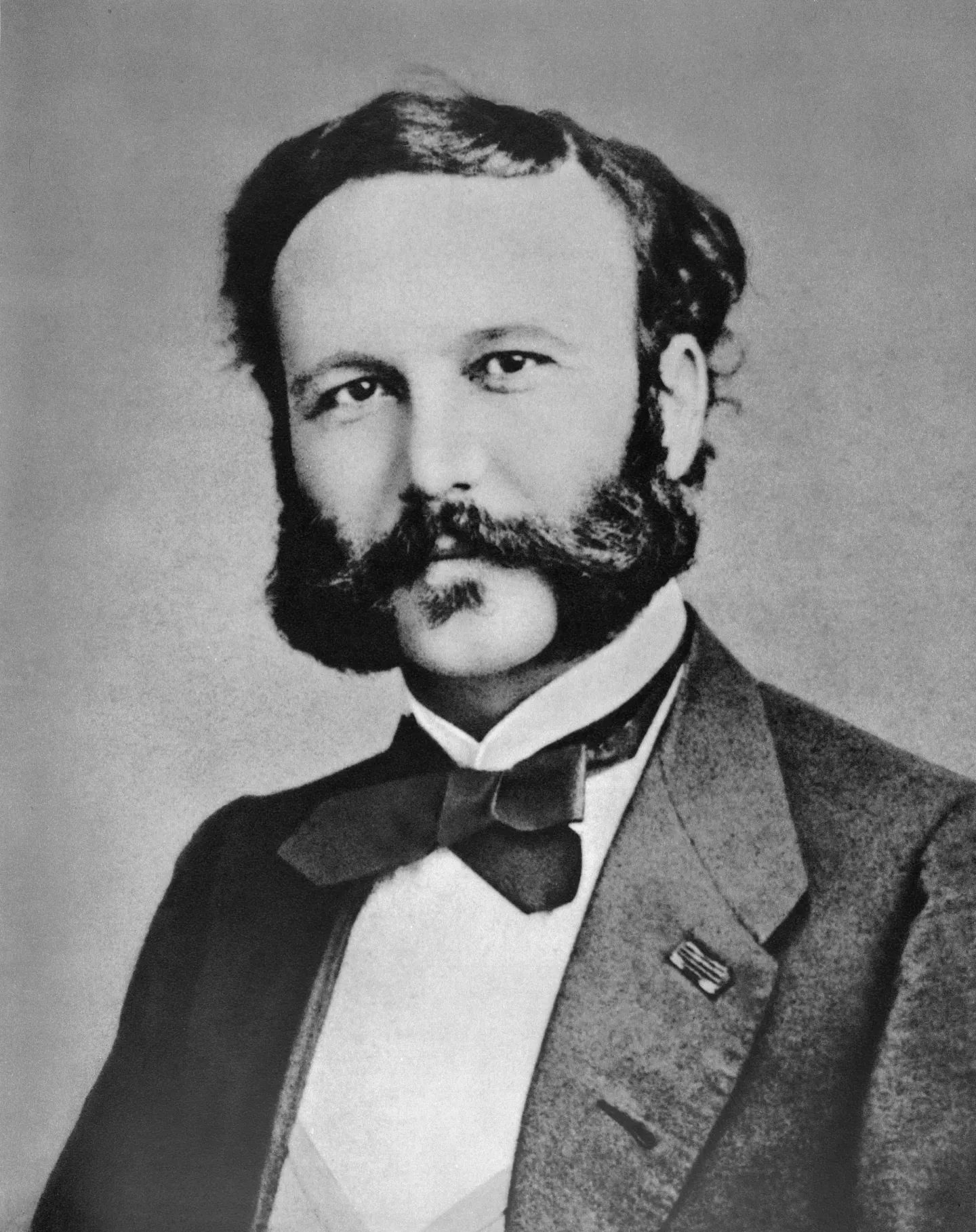 Portrait of Henry Dunant wearing a dark coat and bow tie.