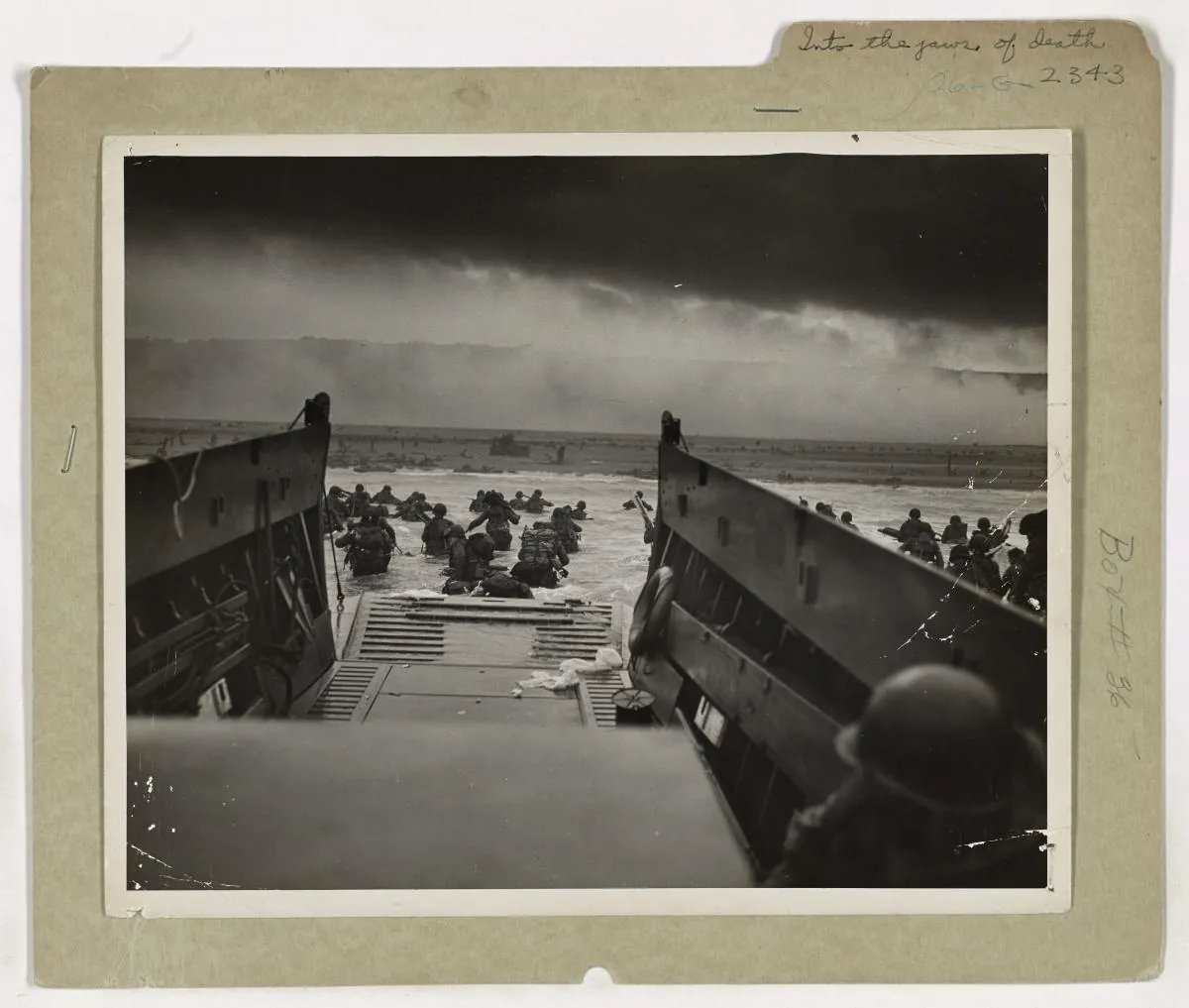 American soldiers wading towards Omaha Beach, seen from inside a landing craft through its open ramp.