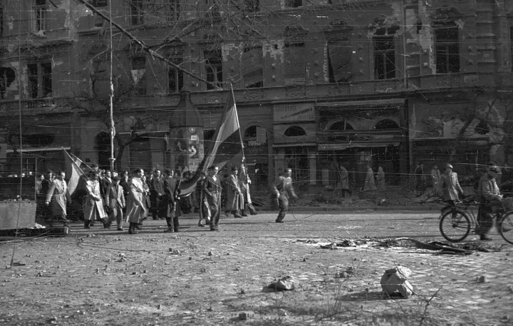 People carrying Hungarian national flags along a rubble-strewn Budapest boulevard during the 1956 revolution