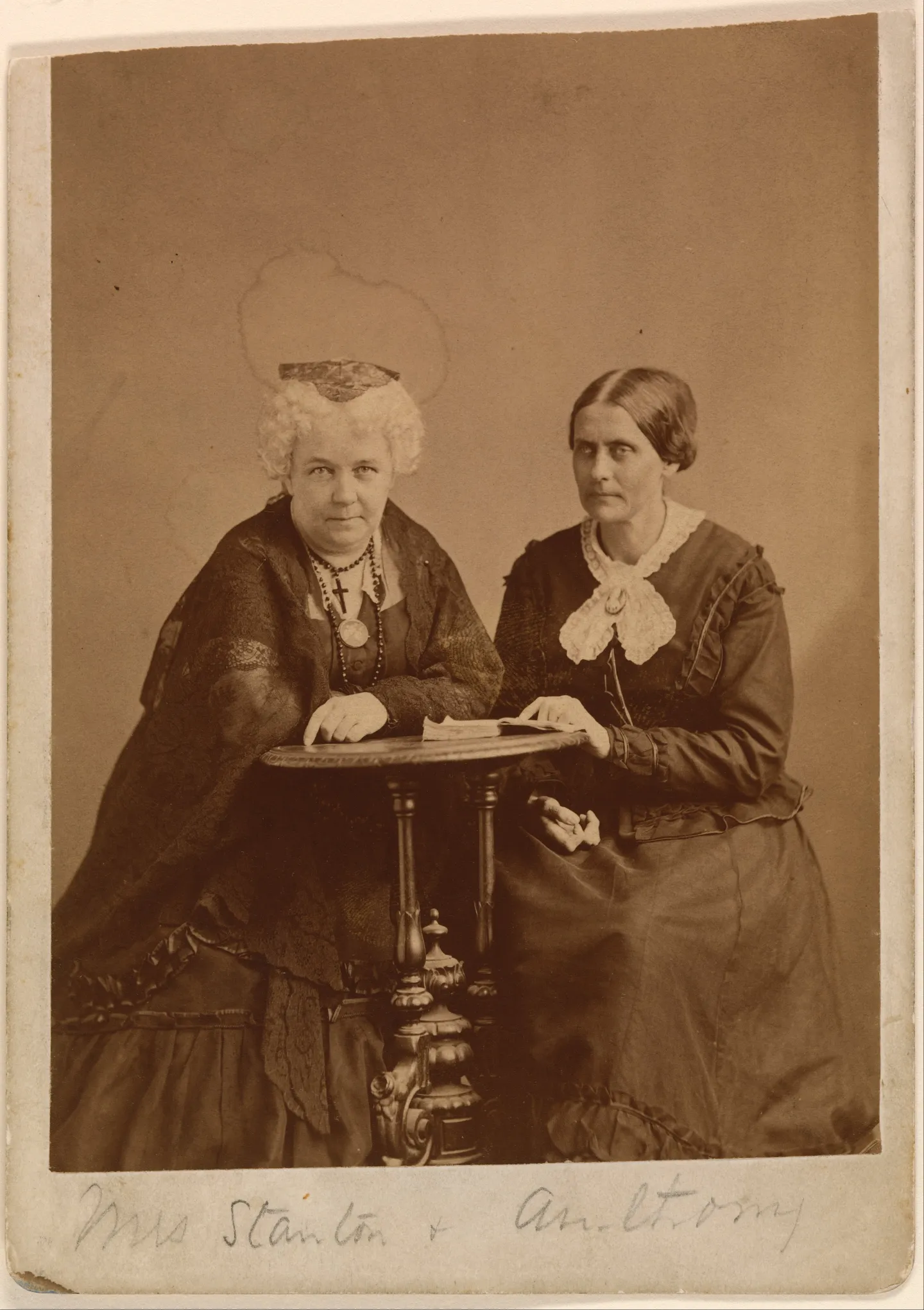 Elizabeth Cady Stanton and Susan B. Anthony seated together beside a table.