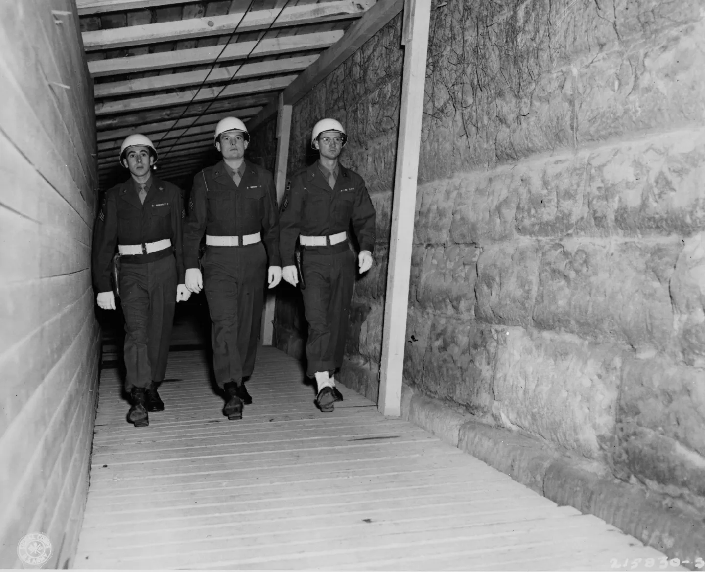 Three uniformed American prison guards walk through a narrow covered passage inside Nuremberg prison.