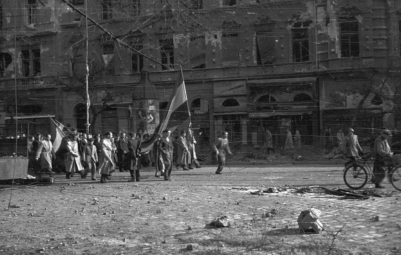 People carrying Hungarian national flags along a rubble-strewn Budapest boulevard during the 1956 revolution