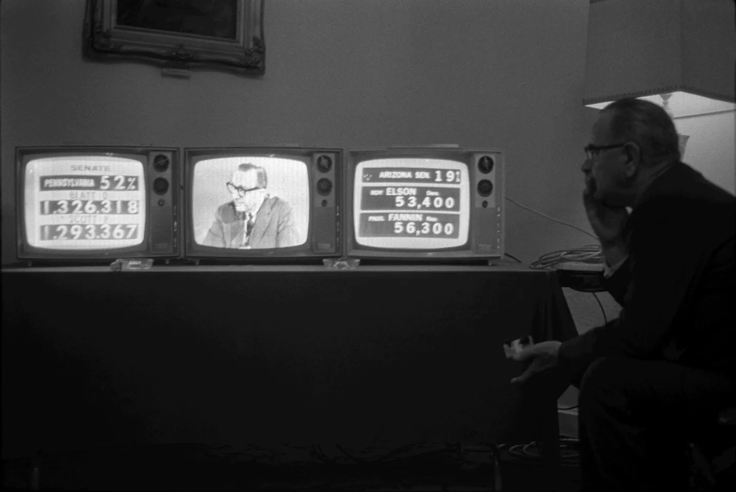Johnson seated beside three television sets showing election coverage.