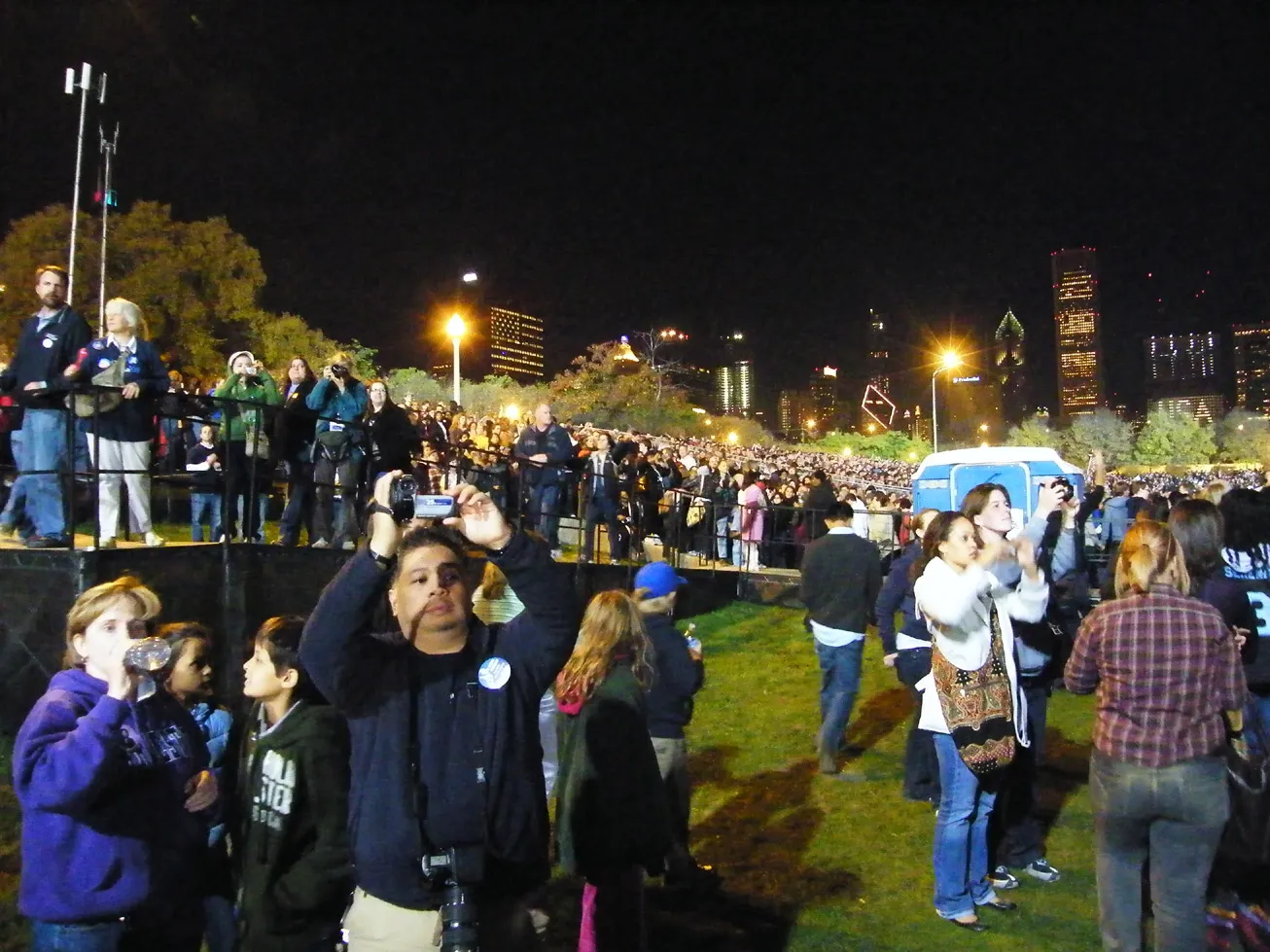 Spectators on the grass in Grant Park, some photographing the nighttime celebration.