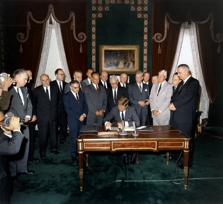 President Kennedy signing the test ban treaty ratification papers surrounded by officials