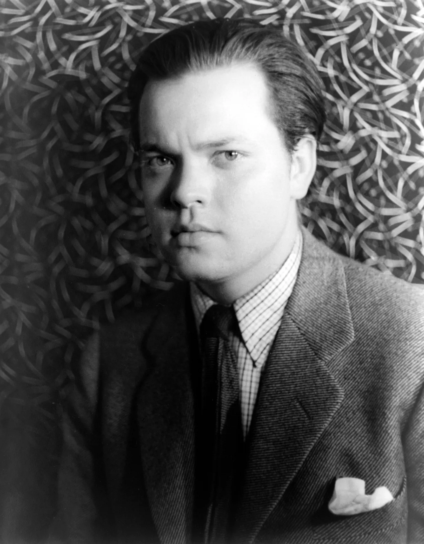 Orson Welles in a jacket and tie, photographed against a patterned background.