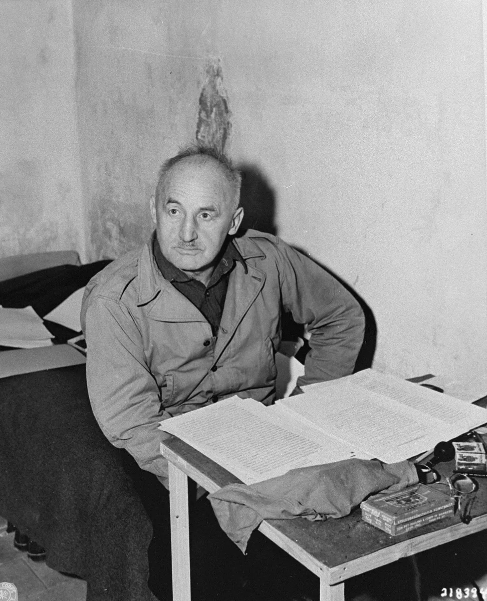 Julius Streicher sits in a prison cell at a small table covered with documents and writing materials.