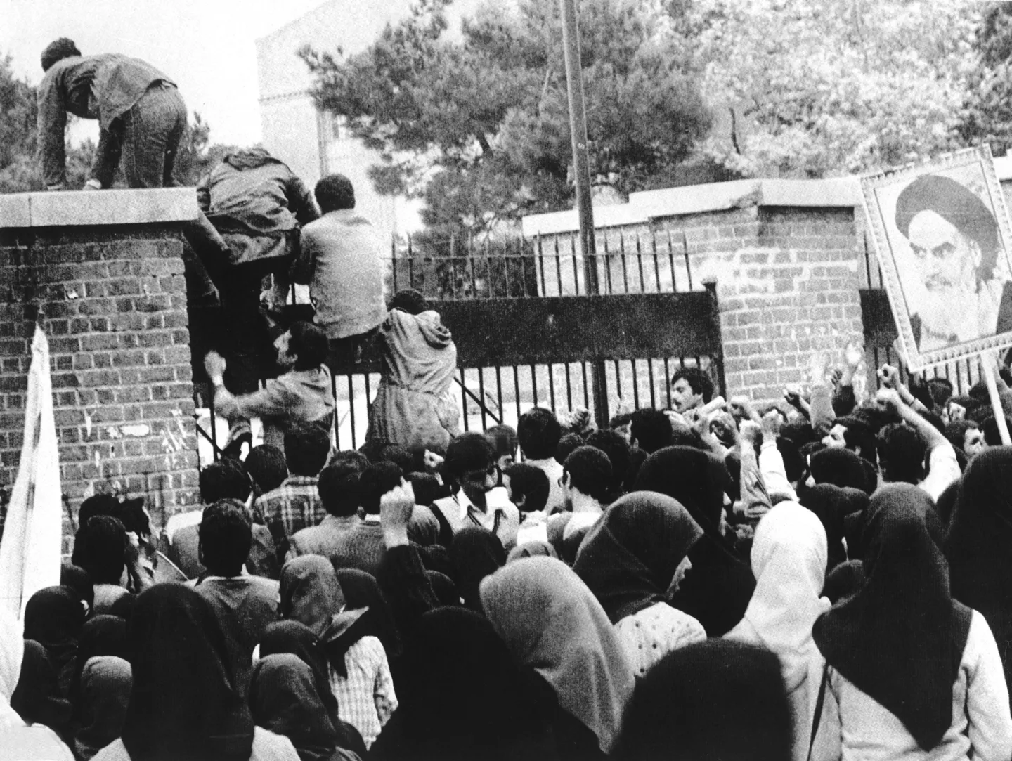 Students climbing a gate above a crowd at the U.S. Embassy in Tehran.