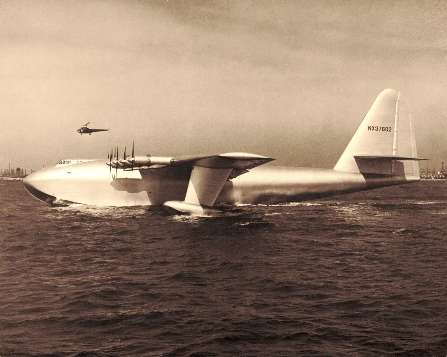 H-4 Hercules flying boat on the water, with an aircraft overhead.