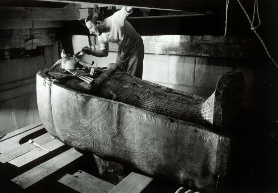 Howard Carter bending over Tutankhamun’s decorated coffin.