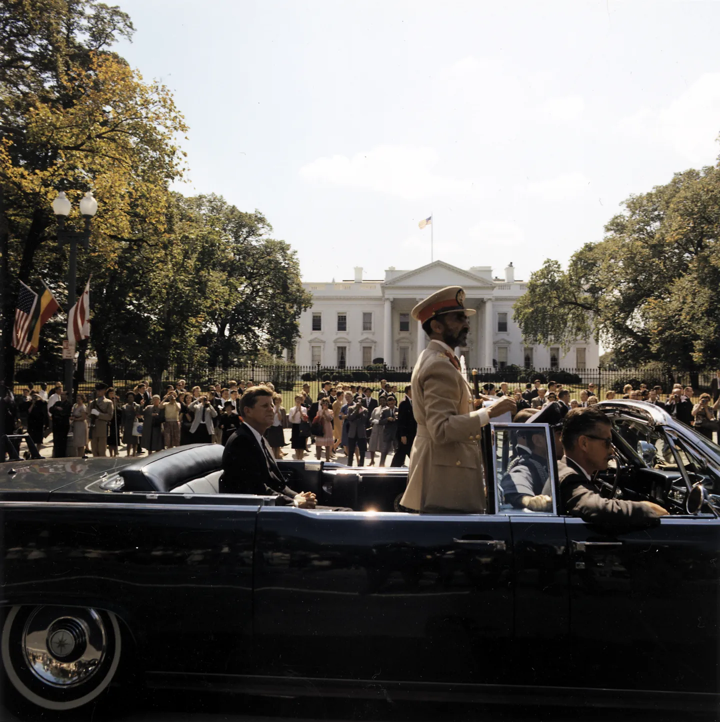 Haile Selassie stands in an open car beside President Kennedy near the White House.