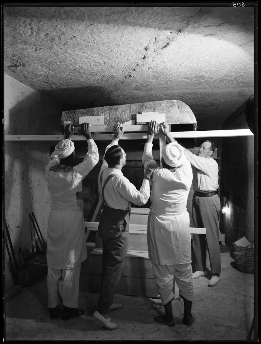 Four men lifting the roof of a burial shrine inside Tutankhamun’s tomb.
