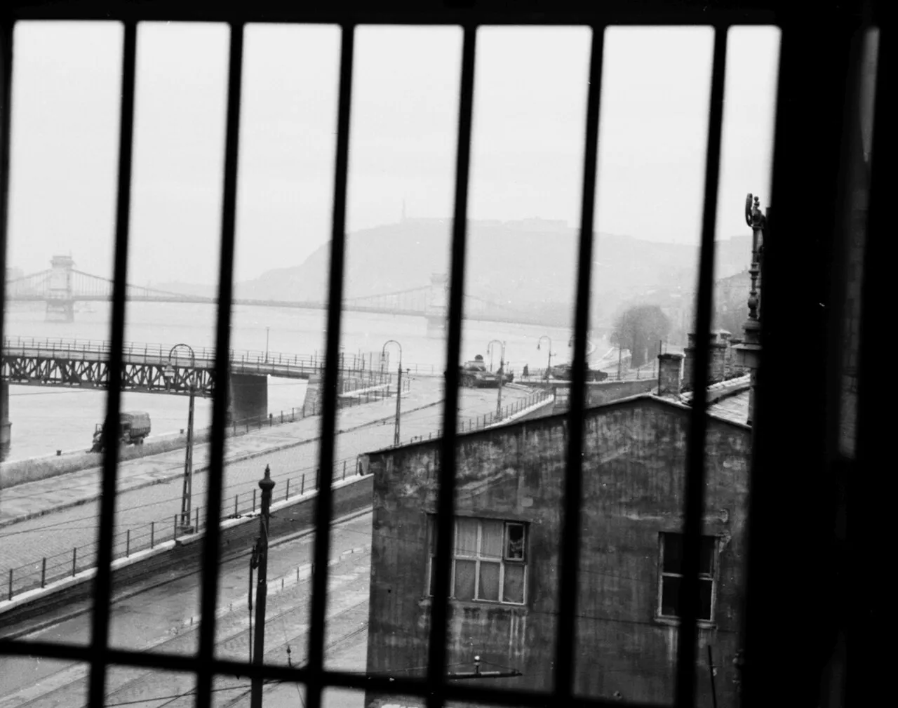 Two tanks near Kossuth Bridge viewed through window bars, with the Danube beyond.