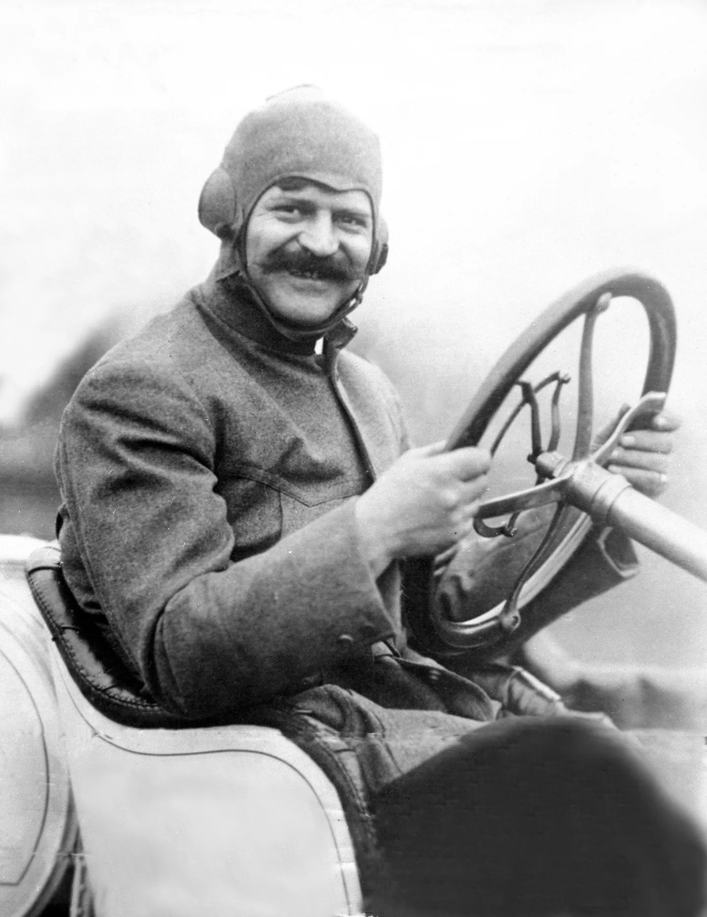 Louis Chevrolet smiles from the driver’s seat of a racing car.