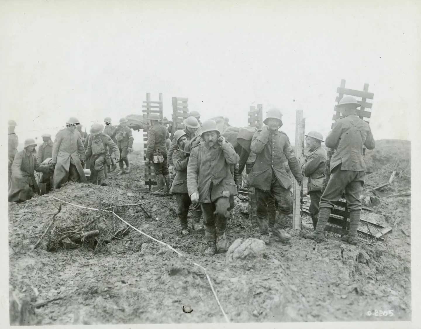 Soldiers carrying wooden trench mats pass men moving wounded troops along a track.