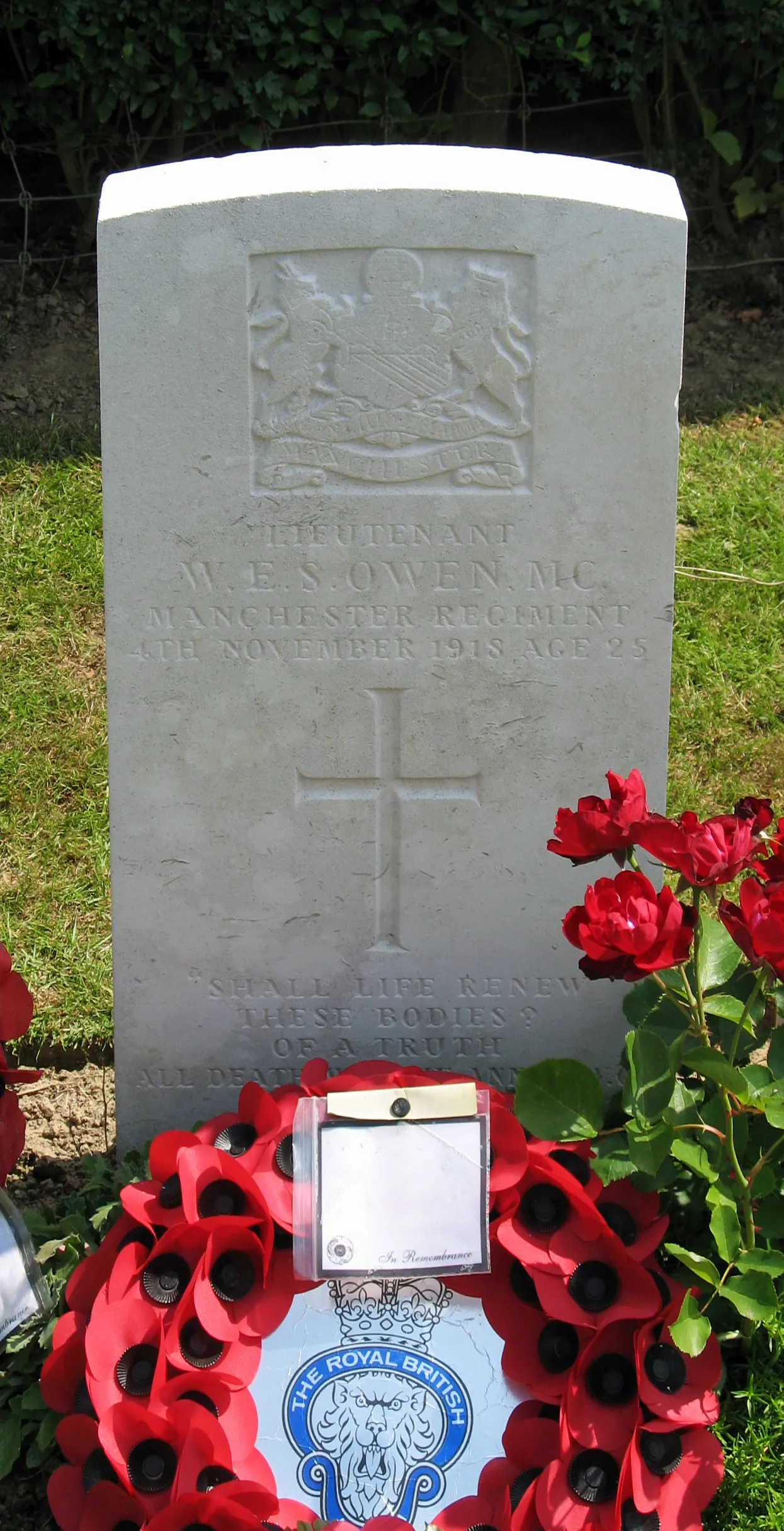 Wilfred Owen’s white military headstone among flowers in the cemetery at Ors.