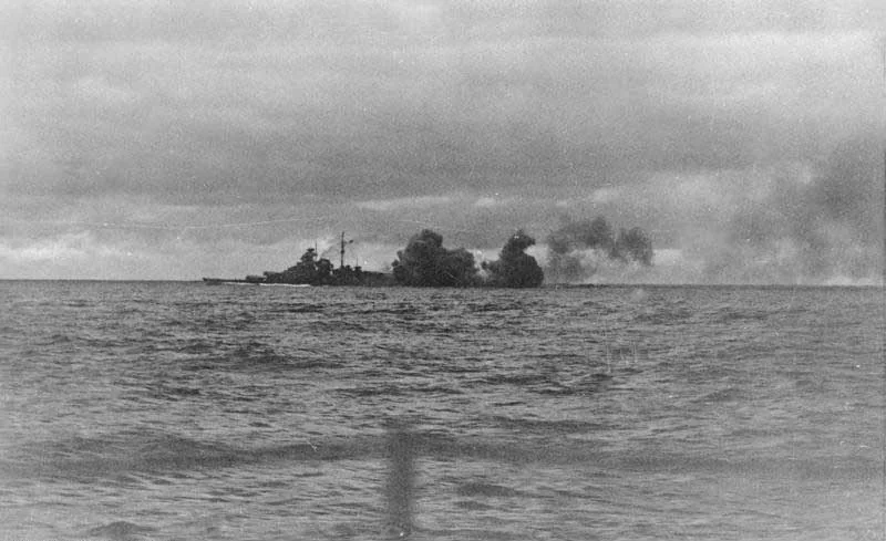 Bismarck firing in the Denmark Strait, her dark silhouette partly obscured by dense gun smoke above the sea.
