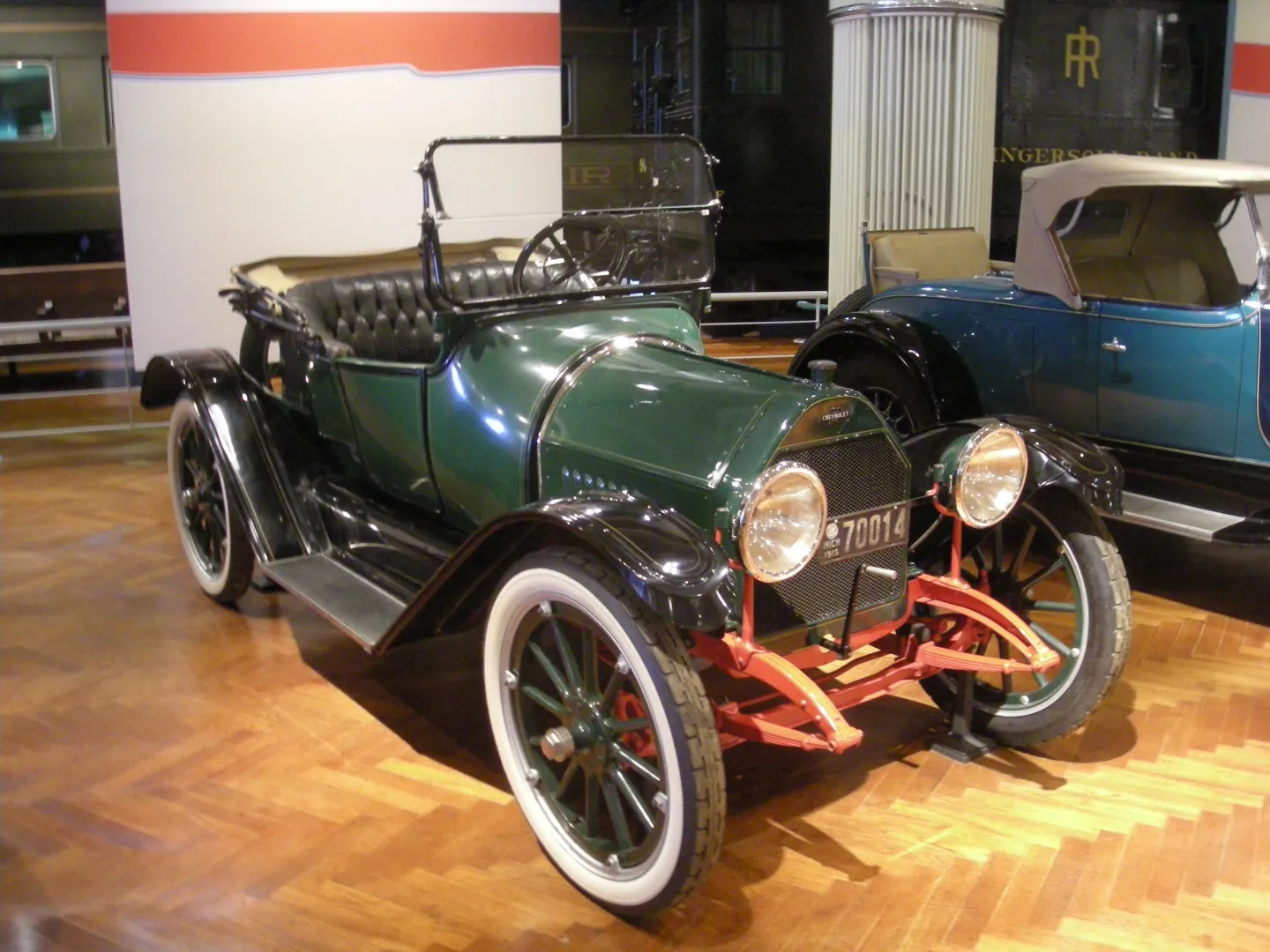 Green 1915 Chevrolet Royal Mail roadster with red wheels on museum display.