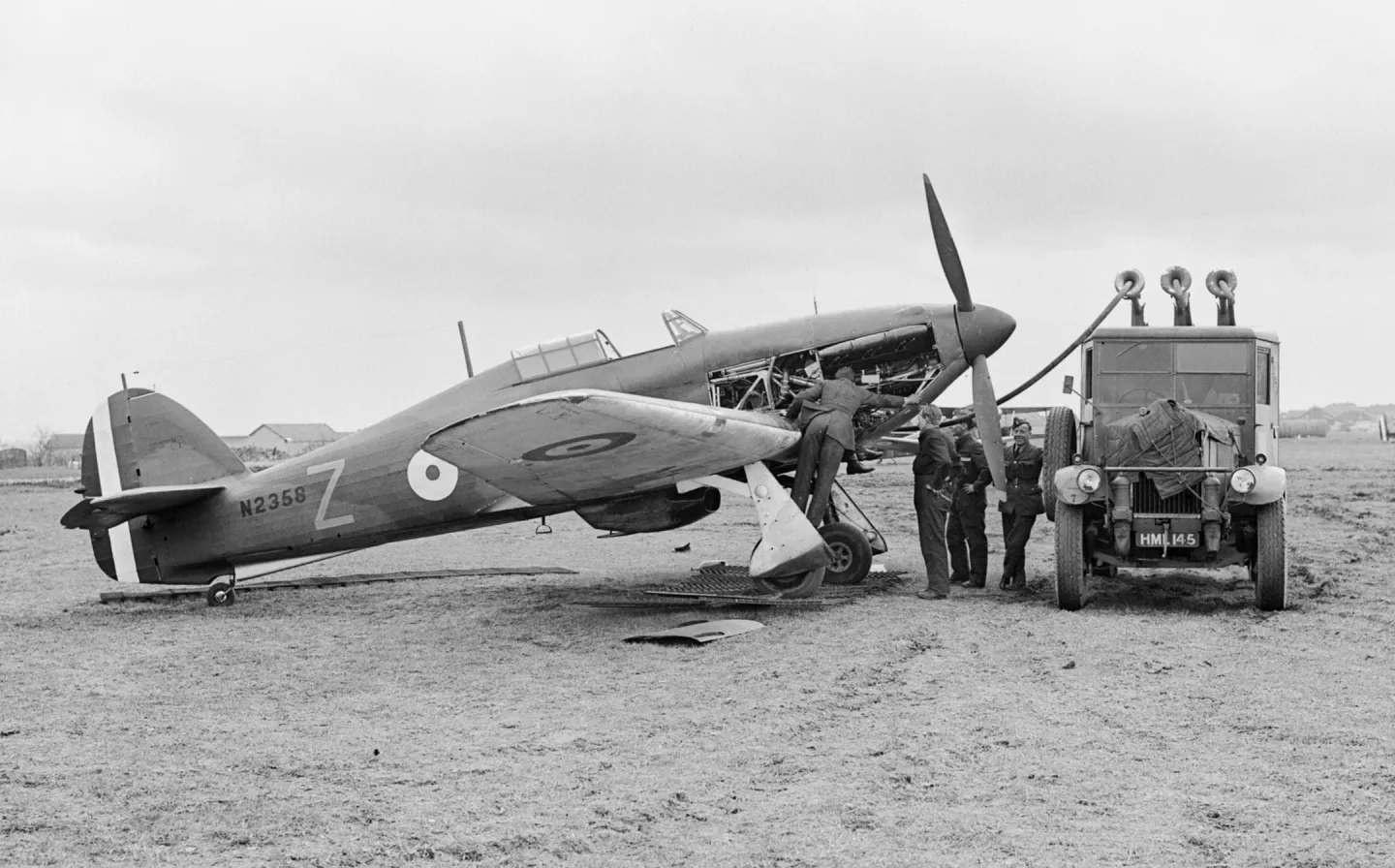 Ground crew servicing and refueling a Hurricane with its engine cowling open.