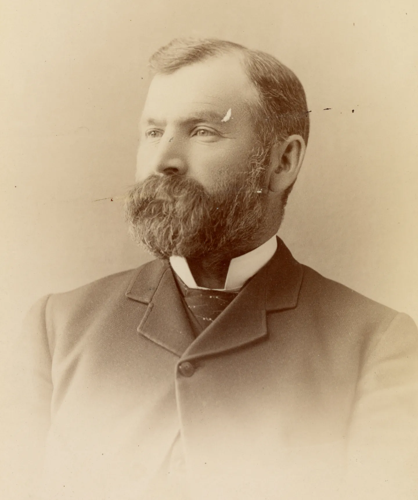 Studio portrait of John Miller with a beard and dark coat.