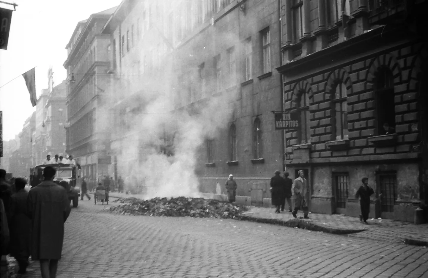 Smoke rising from a heap on Dohány Street while pedestrians pass nearby.