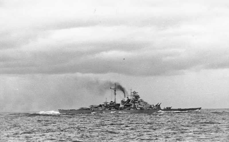 Bismarck steaming across choppy water after the Denmark Strait battle, with smoke trailing from her funnel and the bow pointing right.