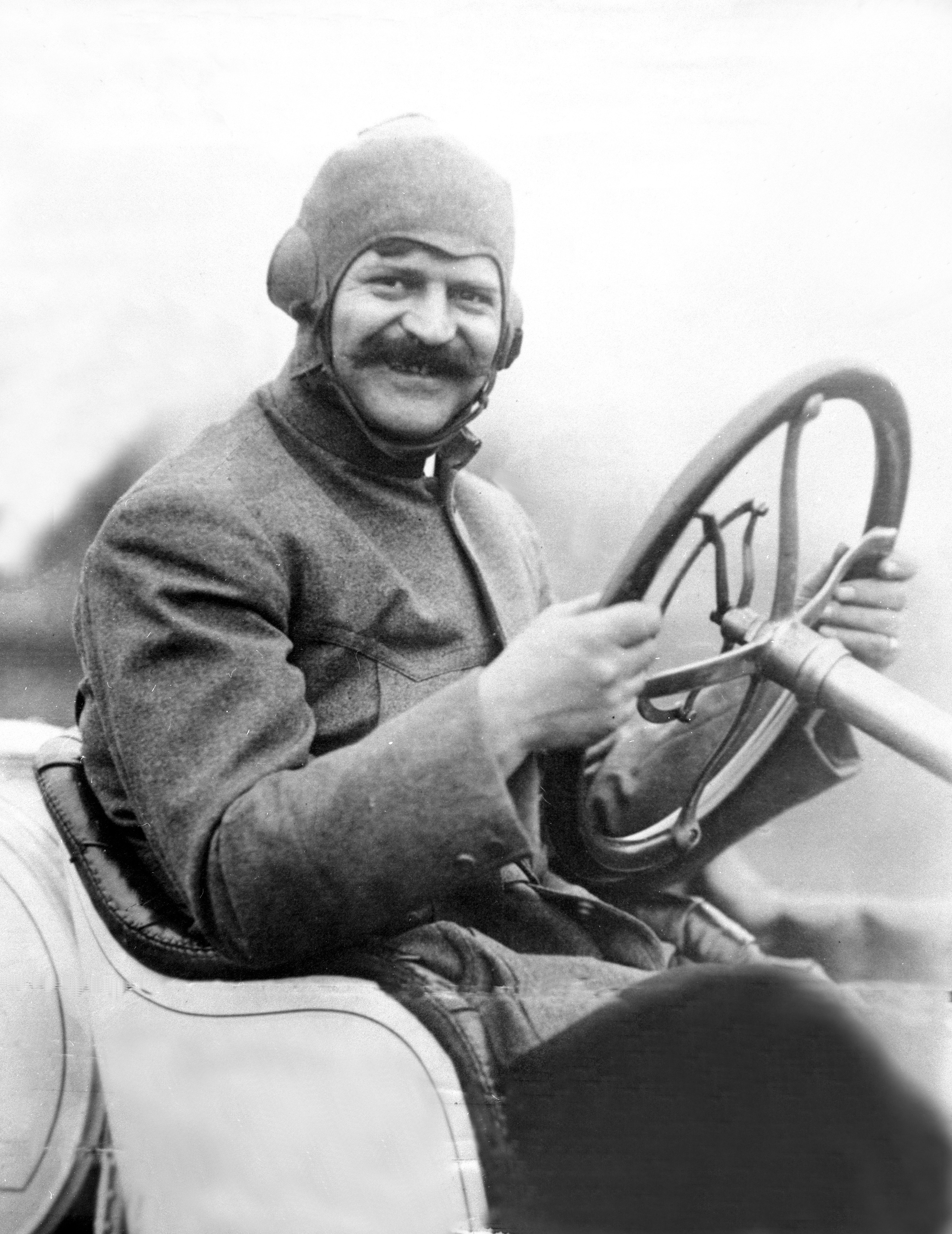 Louis Chevrolet smiles from the driver’s seat of a racing car.